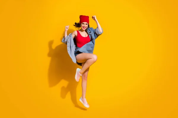 Pełny rozmiar zdjęcie zachwycony szalony młodzieży dziewczyna skok świętować rabat wygrać podnieść pięści krzyczeć tak nosić czerwony nakrycie głowy dżinsowe trampki pojedyncze izolowane na jasny połysk kolor tła — Zdjęcie stockowe