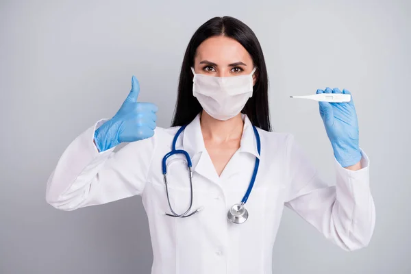 Primer plano retrato de ella ella agradable atractiva chica segura doctora terapeuta sosteniendo en la mano termómetro que muestra pulgar aislado sobre fondo de color pastel gris — Foto de Stock