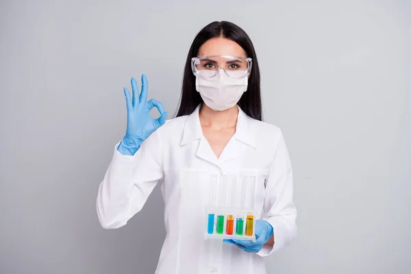 Close-up portrait of her she nice attractive content qualified girl biologist doc holding in hands colorful flasks showing ok-sign ad advert decision isolated over grey pastel color background