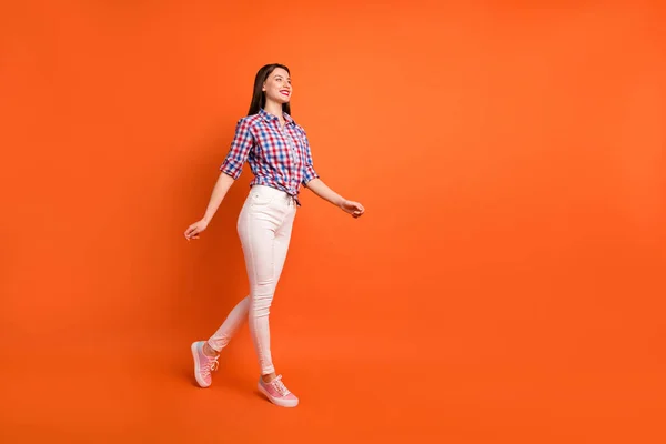 Full length body size view of nice attractive slender cheerful dreamy straight-haired girl wearing checked shirt walking enjoying isolated on bright vivid shine vibrant orange color background — стоковое фото