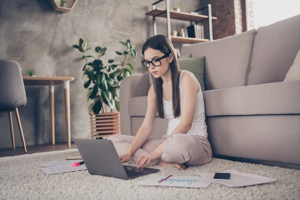 Full length photo of focused smart expert girl sit carpet legs cross work laptop distance have online partners executive colleagues communication analyse statistics in house indoors — Stock fotografie