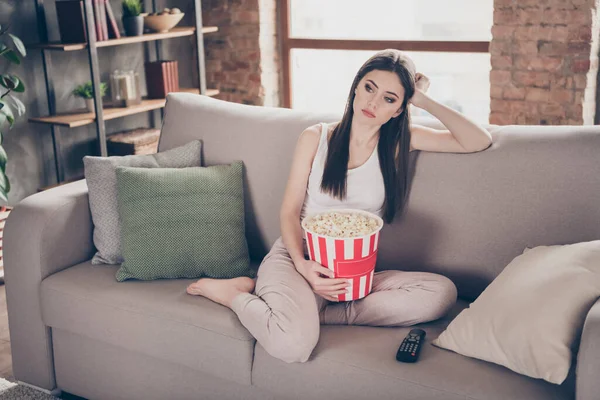 Полная длина фото уставшей скучающей девушки сидеть диван смотреть неинтересный фильм держать поп-кукурузную коробку в гостиной дома в помещении — стоковое фото