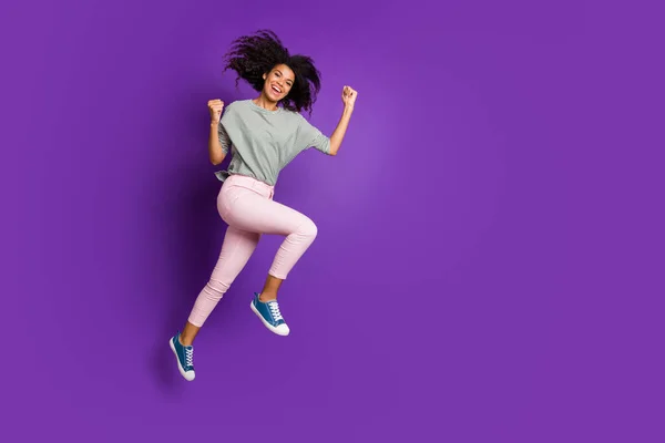 Full length profile side photo of cheerful funky afro American girl jump enjoy discounts win loteria podnieść pięści krzyczeć tak nosić trampki w paski odizolowane fioletowy kolor tła — Zdjęcie stockowe