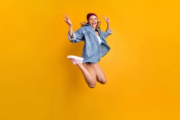 Full längd foto av attraktiv dam lång frisyr gott humör studenter parti hoppa högt upp visar v-tecken symboler bära jeanströja shorts hatt skor isolerad gul färg bakgrund — Stockfoto