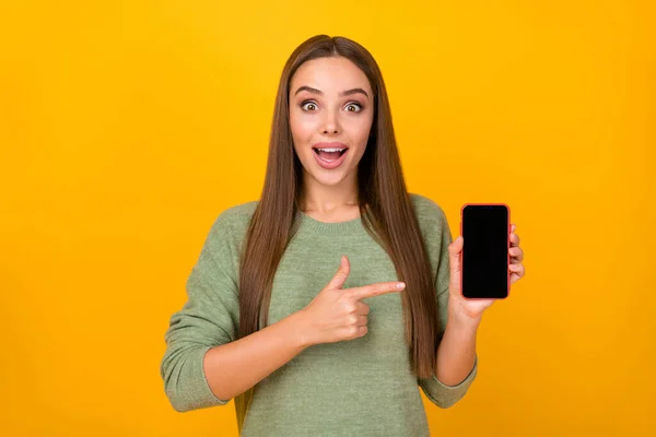 Портрет дивовижно збудженої божевільної дівчини тримає мобільний телефон вражений новими функціями гаджетів, як точковий індексний палець пропонує вибрати джемпер, ізольований на яскравому фоні кольору блиску — стокове фото