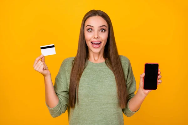 Portrait surprised excited crazy girl demonstrate smartphone hold credit card impressed easy bank paying purchase scream wow omg wear green sweater jumper isolated bright shine color background — Stock Photo, Image