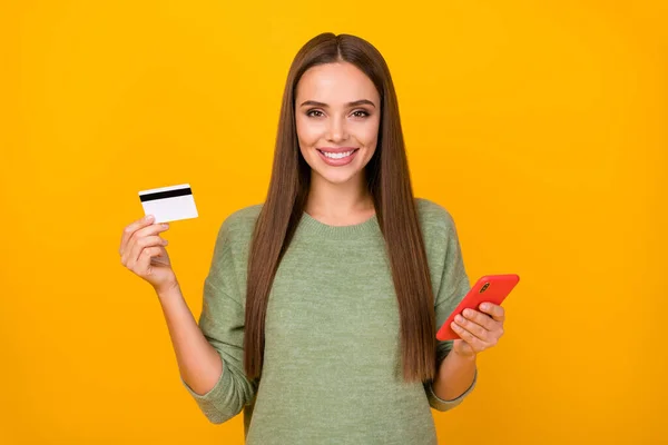 Portrait of positive cheerful girl use cellphone show plastic card social media online banking user payer recommend buy online wear sweater isolated over bright shine color background — Stock Photo, Image