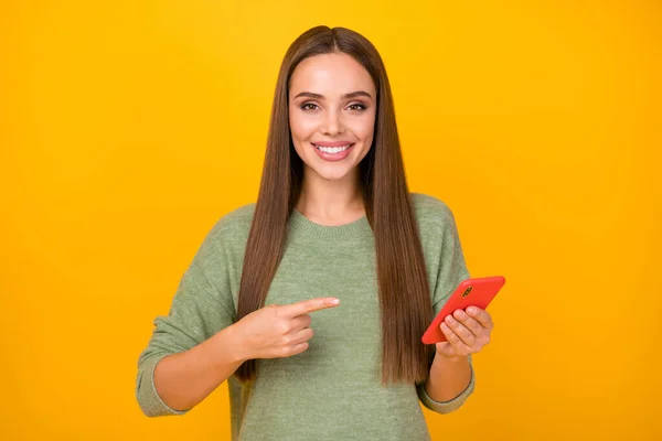 ポジティブな陽気な女の子のプロモーションブロガーの肖像は、携帯電話のポイントインデックス指を使用します現在のソーシャルネットワークの広告は、明るい輝きの色の背景に隔離ジャンパーを着用 — ストック写真