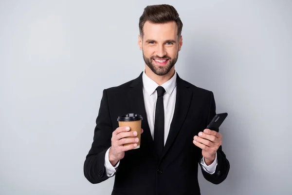 Portrait of positive charming trader man hold take-away americano hot beverage mug use his smartphone always connection concept wear black jacket isolated grey color background — Stock Photo, Image