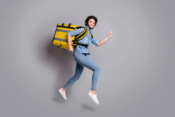 Full body foto positief meisje koerier springen run wil snel leveren maaltijd lunch coronavirus quarantaine dragen thermische container dragen denim jeans shirt helm geïsoleerde grijze kleur achtergrond — Stockfoto