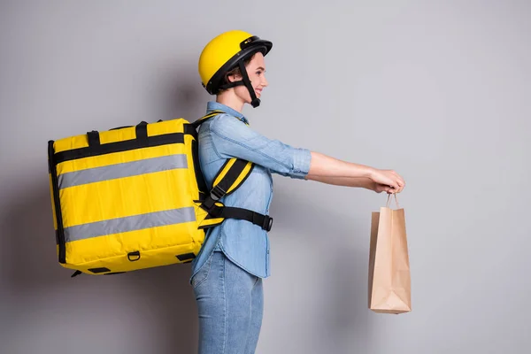 Profil Seite Foto von positiven Mädchen Kurier halten Papierpaket geben Geschenk Lieferung Kunde tragen thermische Rucksack tragen Jeans-Hemd isoliert über graue Farbe Hintergrund — Stockfoto