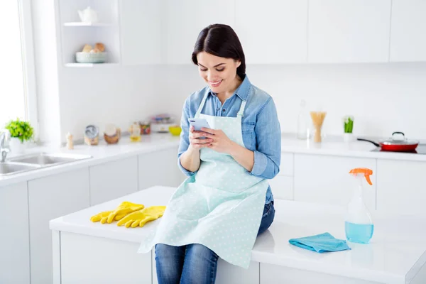 Retrato de mulher alegre positivo tem desinfecção vírus corona cozinha mesa de sentar uso smartphone siga limpeza mídia social notícias informações em casa dentro de casa — Fotografia de Stock