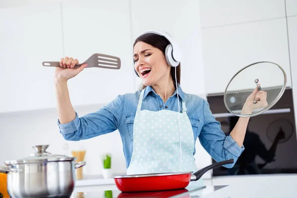 Portret van funky grappig huis vrouw koken avondeten koekenpan luisteren muziek headset stel je voor dat ze beroemde pop ster zingen spatel in huis keuken binnen — Stockfoto