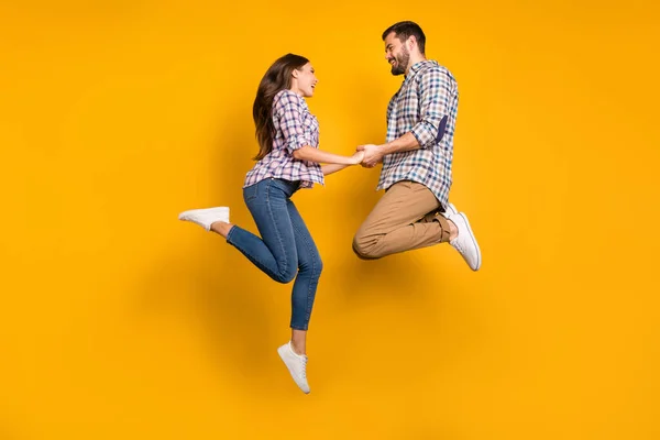 Corpo inteiro foto bonita senhora bonito cara casal pulando alto para cima conhecer aventuras brincalhão segurando braços desportivo pessoas usam casual xadrez camisas jeans calças sapatos isolados cor amarela fundo — Fotografia de Stock