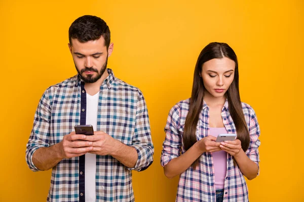 Foto aantrekkelijke dame knappe man achteloos paar kijken telefoon scherm negeren elkaar verslaafde gebruikers dragen casual geruite shirts outfit geïsoleerde gele kleur achtergrond — Stockfoto