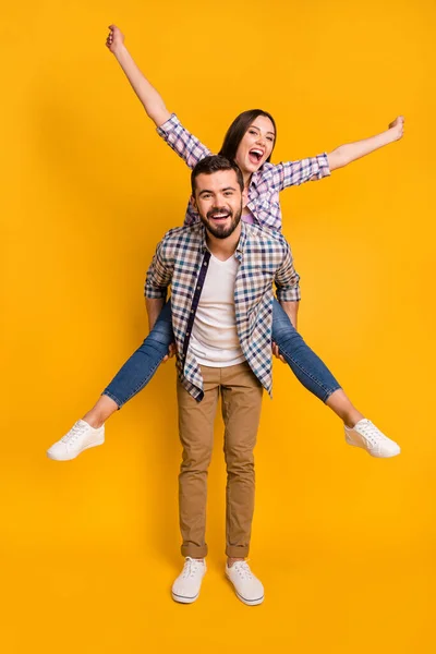 Corpo inteiro vertical foto bonita senhora bonito cara casal transportar piggyback conhecer aventuras brincalhão espalhar braços como asas desgaste casual xadrez camisas calças isoladas cor amarela fundo — Fotografia de Stock