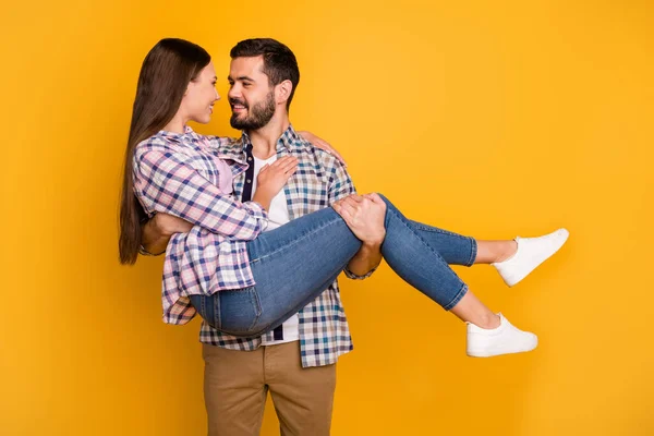 Foto av vacker dam stilig kille par just gift man hålla brud fru armar bära smekmånad bil överraskning resa resa bära casual rutig skjortor jeans isolerad gul färg bakgrund — Stockfoto