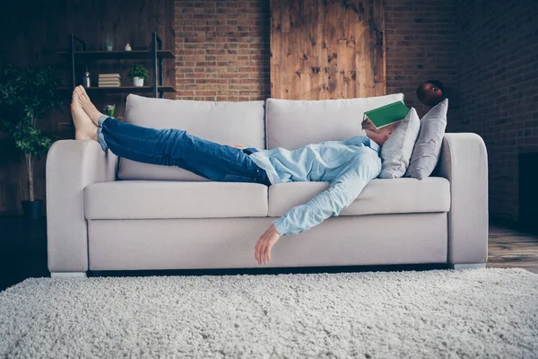 Teljes méretű profil fotó a hazai jóképű srác marad otthon karantén idő elalvás olvasó könyv borító arc fekvő mezítlábas kényelmes kanapé álmodozó modern belső nappali beltérben — Stock Fotó