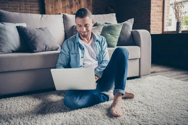 Foto de chico guapo hogareño relajante sentado cómoda alfombra mullida cerca del sofá portátil de navegación freelancer trabajo remoto quedarse en casa buen humor cuarentena tiempo fin de semana sala de estar en el interior —  Fotos de Stock