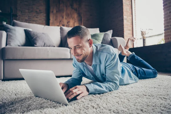 Primer plano foto de chico guapo hogareño relajante tumbado cómoda alfombra mullida cerca de sofá portátil de navegación freelancer trabajo remoto quedarse en casa buen humor cuarentena tiempo sala de estar en el interior —  Fotos de Stock