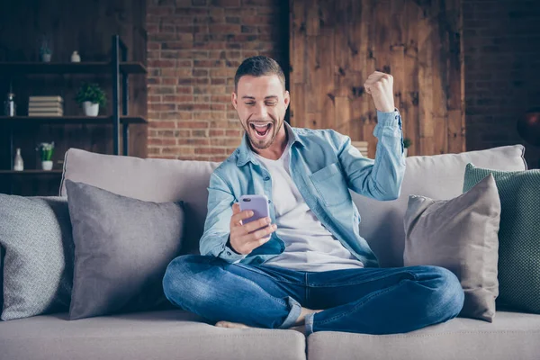 Foto van knappe man thuis blijven quarantaine tijd houden telefoon blogger freelancer goed humeur check houdt volgelingen benen gekruist zitten comfortabele bank modern interieur woonkamer binnen — Stockfoto