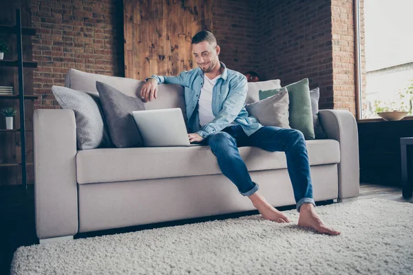 Photo of handsome homey barefoot guy relaxing sitting comfy couch browsing notebook freelancer remote work staying home good mood quarantine time living room indoors — Stock Photo, Image