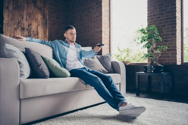 Perfil foto do cara bonito doméstico relaxante sentar sofá confortável ficar em casa bom humor sonhador quarentena tempo assistir televisão mudar canais moderno interior sala de estar dentro de casa — Fotografia de Stock