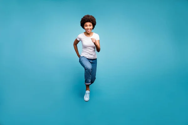 Foto de larga duración de la piel oscura funky dama ondulada saltando alta persona deportiva corriendo de compras final negro viernes desgaste casual blanco camiseta jeans aislados color azul fondo —  Fotos de Stock