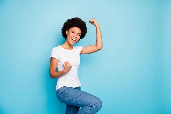 Photo of funny dark skin curly lady holding fists near chest worried supporting friends sportive competition wear casual white t-shirt jeans isolated blue color background — Stock Photo, Image