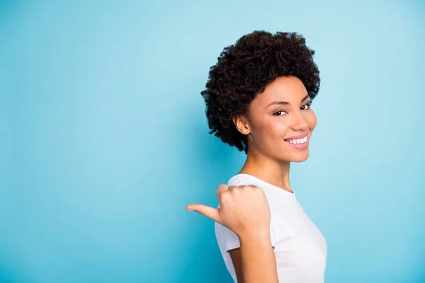 Foto de primer plano de la hermosa mujer rizada de piel oscura gerente de ventas que indica el dedo pulgar del lado del espacio vacío precios de venta ropa casual camiseta blanca aislado fondo de color azul — Foto de Stock