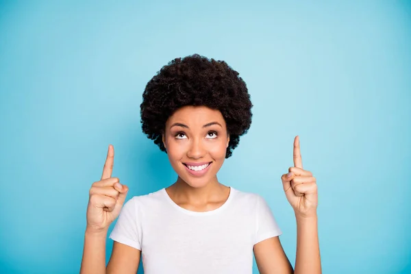 Close-up foto van mooie donkere huid krullende dame sales manager aangeeft vingers op zoek naar lege ruimte lage prijzen winkelen dragen casual wit t-shirt geïsoleerde blauwe kleur achtergrond — Stockfoto