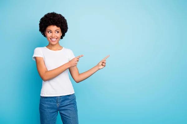 Foto di bella pelle scura razza mista ondulato signora direttore vendite indicando dita spazio vuoto prezzi bassi shopping usura casual bianco t-shirt jeans isolato blu colore sfondo — Foto Stock