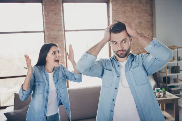 Foto de mujer indignada gritar hombre tiene conflicto malentendido marido tocar las manos cabeza sorprendida esposa reacción stand cerca de confort acogedor sofá en casa en el interior — Foto de Stock