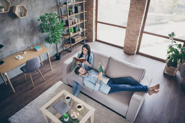 Arriba arriba alto ángulo vista longitud completa foto de pareja enfocada mujer sentarse sofá hombre mentira cabeza rodillas leer interesante libro en casa interior habitación — Foto de Stock