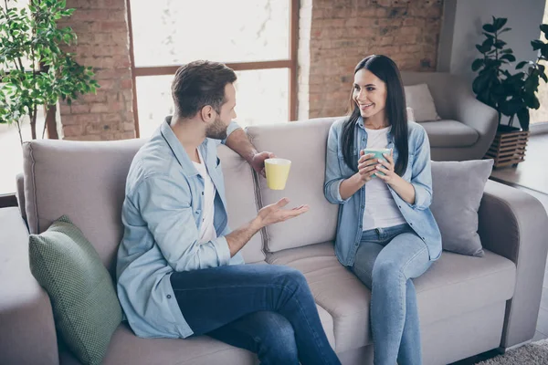 Portrait of positive loving married couple man woman have talk enjoy free time drink cappuccino cup sit couch in house indoors — Stock Photo, Image