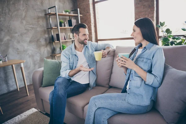 Portrait of positive married couple man woman have talk hold latte coffee cup enjoy free time sit couch in house indoors — Stock Photo, Image