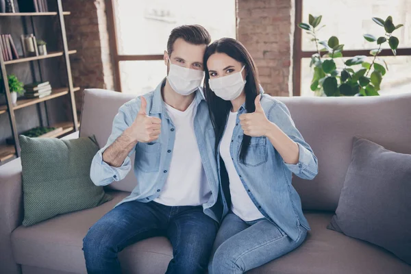 Portrait of positive two people married couple stay home want cov infection epidemic protection wear medical mask recommend show thumb up sign in house indoors — Stock Photo, Image