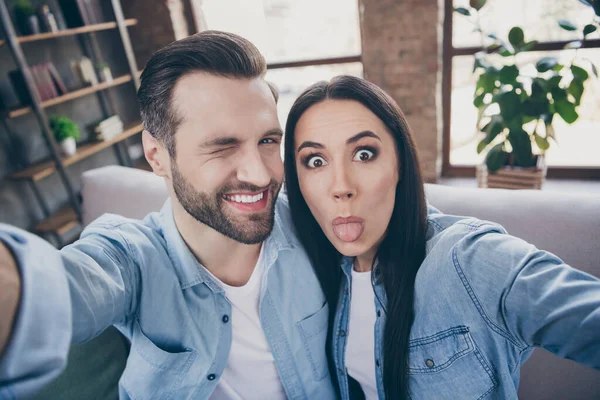 Close up foto de despreocupado brincalhão positivo duas pessoas homem viagem mulher fazer selfie mostrar língua piscar piscar sentar sofá em casa dentro de casa — Fotografia de Stock