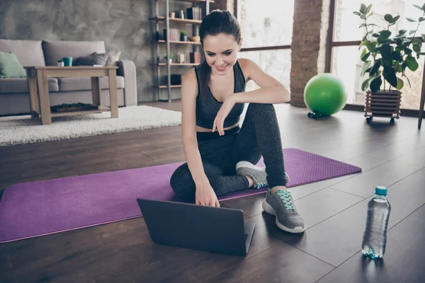 Full body photo of positive active sportive girl sit floor rest relax use laptop search gymnastics flexibility agility exercise in house indoors