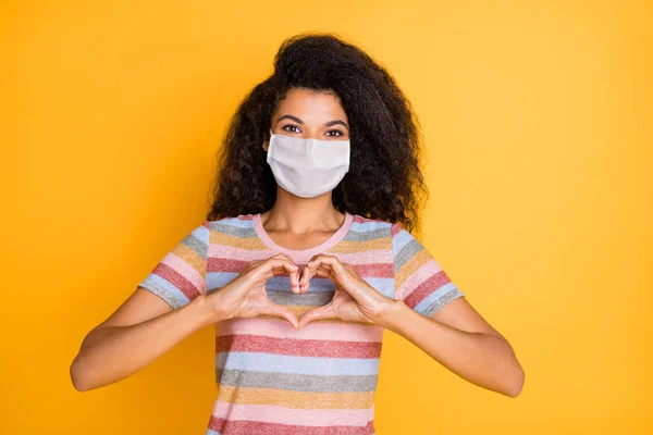Κοντινό πλάνο πορτρέτο της αυτή ωραία υγιή κυματιστά μαλλιά κορίτσι φορώντας μάσκα ασφαλείας που δείχνει το σχήμα της καρδιάς γρίπη Grippe μόλυνση απομονωμένο φωτεινό έντονο λαμπερό κίτρινο χρώμα φόντο — Φωτογραφία Αρχείου