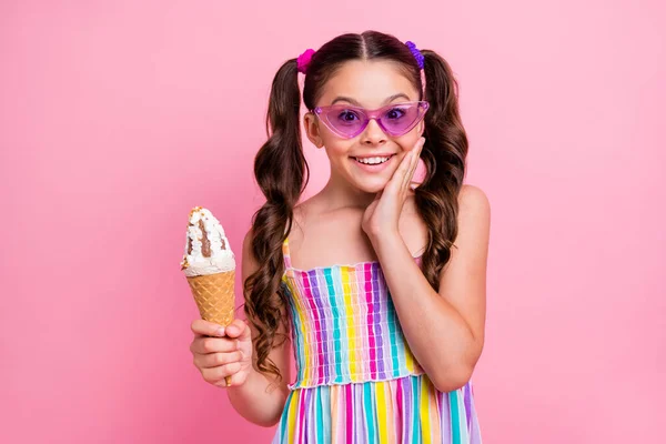 Photo of beautiful little lady two cute curly long tail hold big cone fagylalt gelato hand on face delicious wear cool sun specs színes nyári ruha elszigetelt pasztell rózsaszín háttér — Stock Fotó