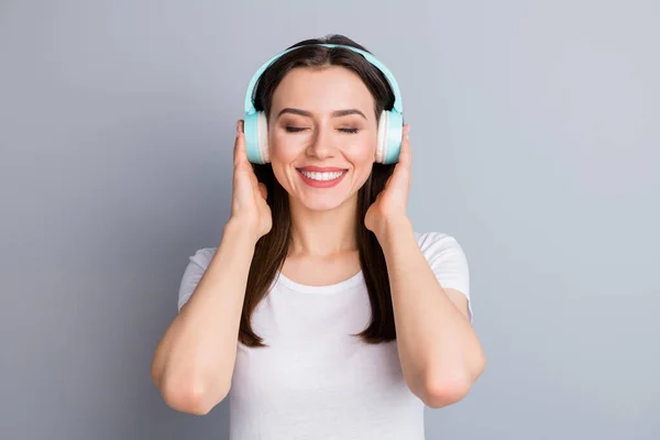 Retrato de la joven alegre positiva mantenga auriculares inalámbricos escuchar música de estilo disco sentir contenido expresión de la cara usar ropa de buen aspecto aislado sobre fondo de color gris — Foto de Stock