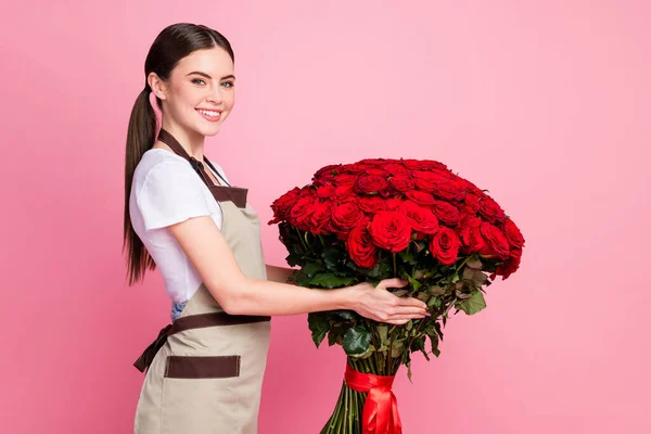 Profile side view portrait of her she nice attractive pretty cheerful cheery girl manager seller holding in hands large big bunch red roses Valentine day isolated on pink pastel color background