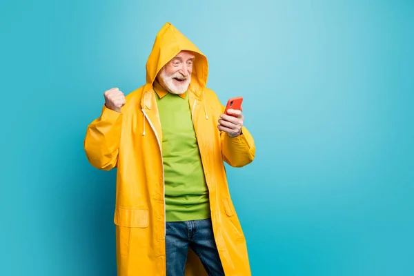 Portrait von seinem netten fröhlich fröhlich zufriedenen grauhaarigen Mann mit gelbem Mantel mit Mobiltelefon schnelle Internetverbindung isoliert auf hellem lebendigen Glanz lebendigen blauen Farbhintergrund — Stockfoto