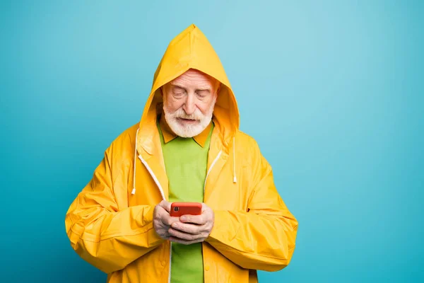 Yakın plan portresi. İyi odaklanmış, beyaz saçlı, sarı palto giyen, cep telefonu kullanan, canlı, parlak, mavi arka planda izole edilmiş web servisi kullanan bir adam. — Stok fotoğraf