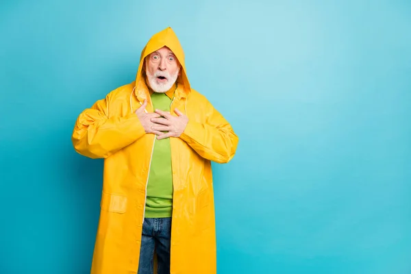 Retrato de su agradable atractivo asustado asombrado hombre de pelo gris con capa amarilla ciclón noticias reacción ataque al corazón aislado en brillante brillo vivo vibrante fondo de color azul —  Fotos de Stock