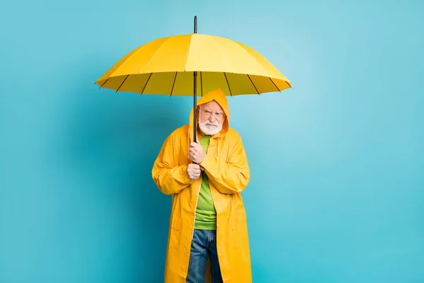 Portrait von ihm irritiert er genervte grauhaarige Mann mit gelben Mantel versteckt unter Sonnenschirm schlechtes kaltes nasses Wetter Zyklon isoliert über hellem lebendigen Glanz leuchtenden blauen Farbhintergrund — Stockfoto