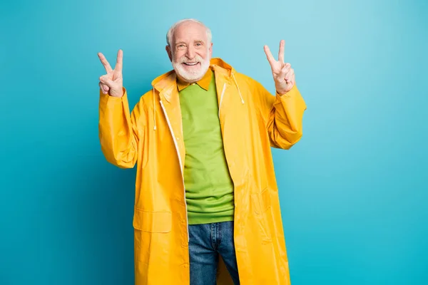 Portrait de son homme aux cheveux gris joyeux et joyeux portant un manteau en plastique jaune montrant un double signe en V isolé sur un fond de couleur bleu vif brillant et vif — Photo