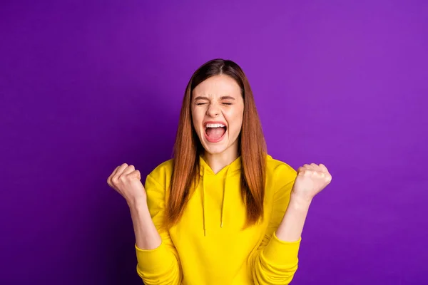 Foto av attraktiv galen dam firar fantastiska prestation höja nävar glädje skrikande bära casual ljusa gula huvtröja isolerad violett färg bakgrund — Stockfoto