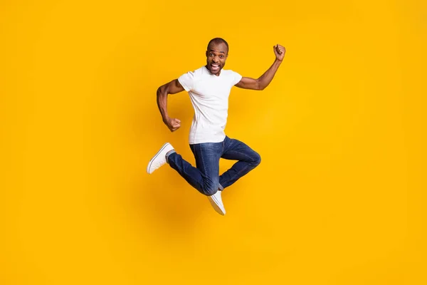 Full size photo of cheerful delighted afro american guy jump celebrate discount spring time win raise fists scream yes wear denim jeans white isolated over shine color background — Stock Photo, Image